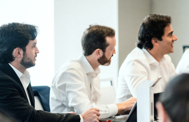 A photo of people sitting at a table looking to the front of the room