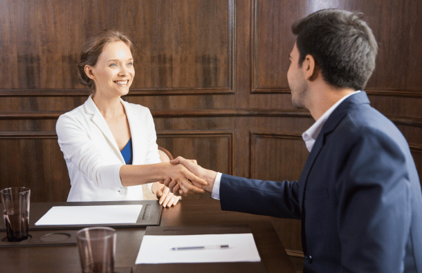 A photo of two business people shaking hands over a wooden desk in an office.