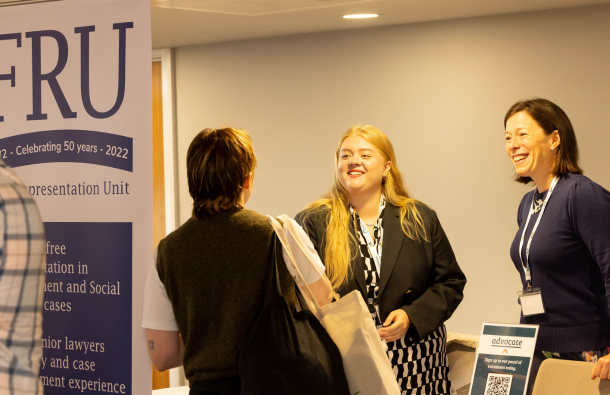 A photo of three people talking and smiling near a banner at an exhibition space