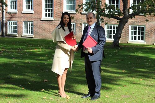 Pauline Chase and Mark Fenhalls KC standing in a courtyard in the shade of trees, smiling and shaking hands. Both are holding red folders.