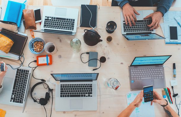 Desk with multiple laptops and headphones as people work.