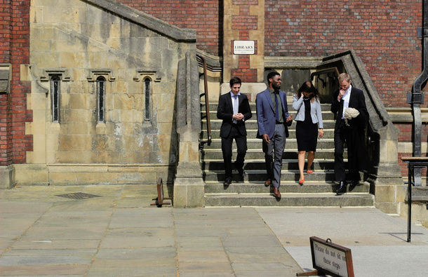 Four people descending stairs outside an old building, one of them is holding a barrister's wig