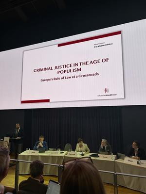 A photo of a panel of people sitting under a big screen that has the title of a presentation: Criminal justice in the age of populism