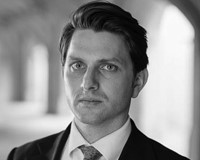 Head and shoulders black and white photograph of barrister Paul Adams. Behind him is a blurred background of an archway.