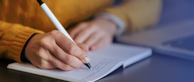 A photo of someone writing in a notebook on a desk