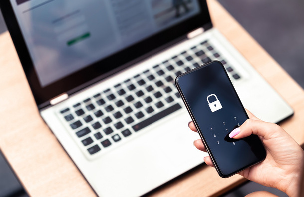 Laptop and a mobile phone held by a person with a lock on the screen, indicating two-factor authentication