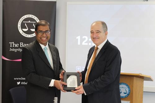 Saliya Pieris and Mark Fenalls KC smiling and shaking hands and holding a silver presentational gift. The navy Bar Council pull up banner is in the background.