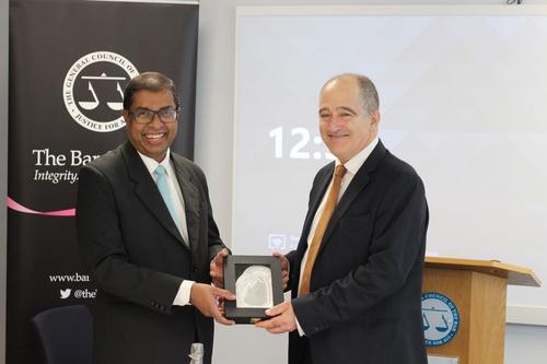 Saliya Pieris and Mark Fenalls KC smiling and shaking hands and holding a silver presentational gift. The navy Bar Council pull up banner is in the background. 