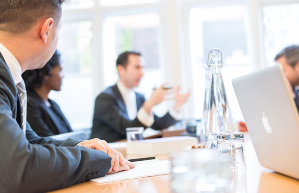 a photo of a group of 4 or more people sitting around a table, with papers and laptops on it,  in discussion